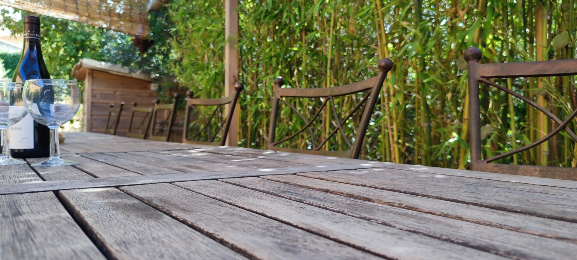 Grande table extérieure en bois sous la pergola, prête pour des repas conviviaux en groupe, jardin méditerranéen, esprit slow tourisme et convivialité.