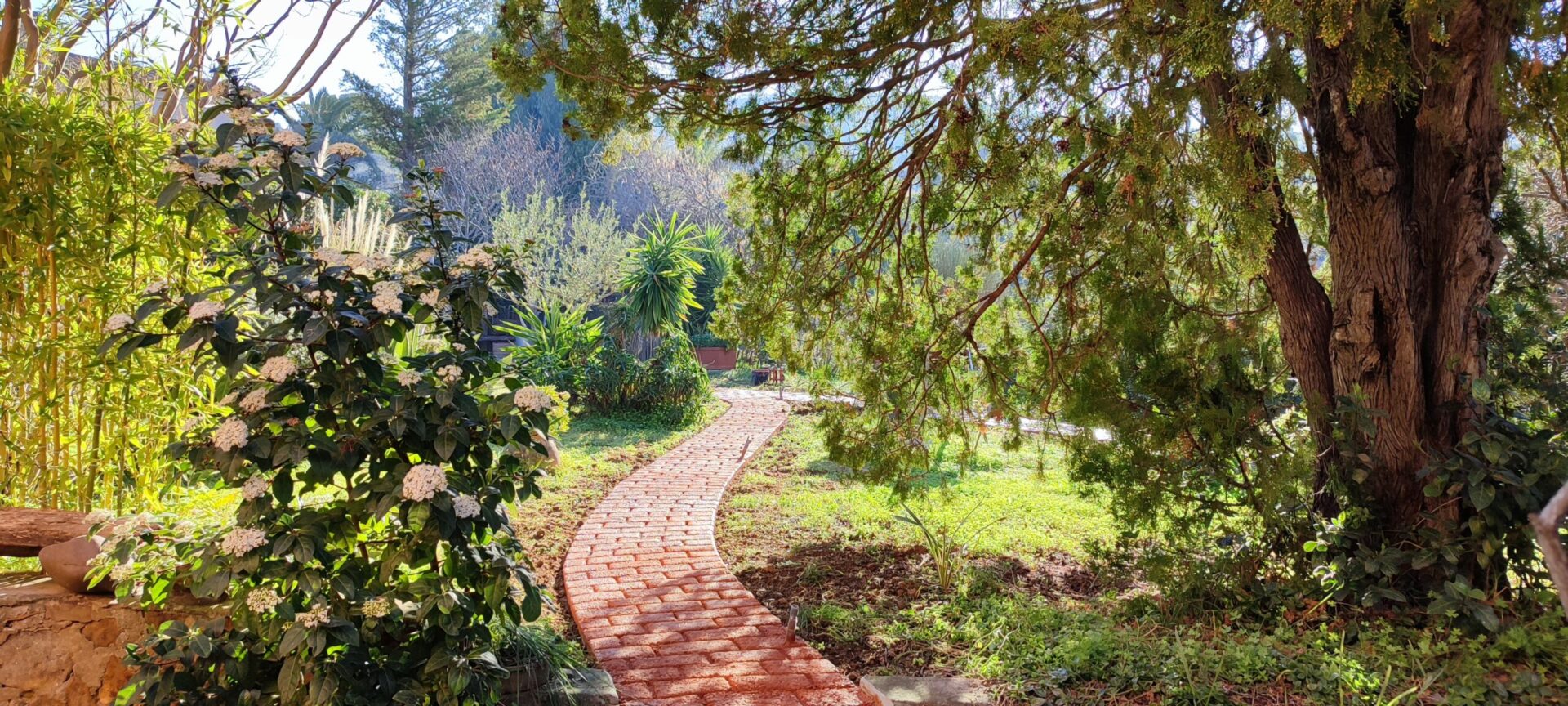 Chemin d'accès en matériaux recyclés serpentant harmonieusement à travers un jardin verdoyant, illustrant l'approche éco-responsable du Mas de la Gavaresse au Pradet.