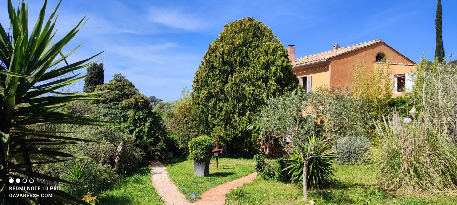 Façade sud-est du Mas de la Gavaresse, villa provençale en pierre avec ses volets ouverts et ses terrasses ensoleillées, intégration dans le paysage méditerranéen.