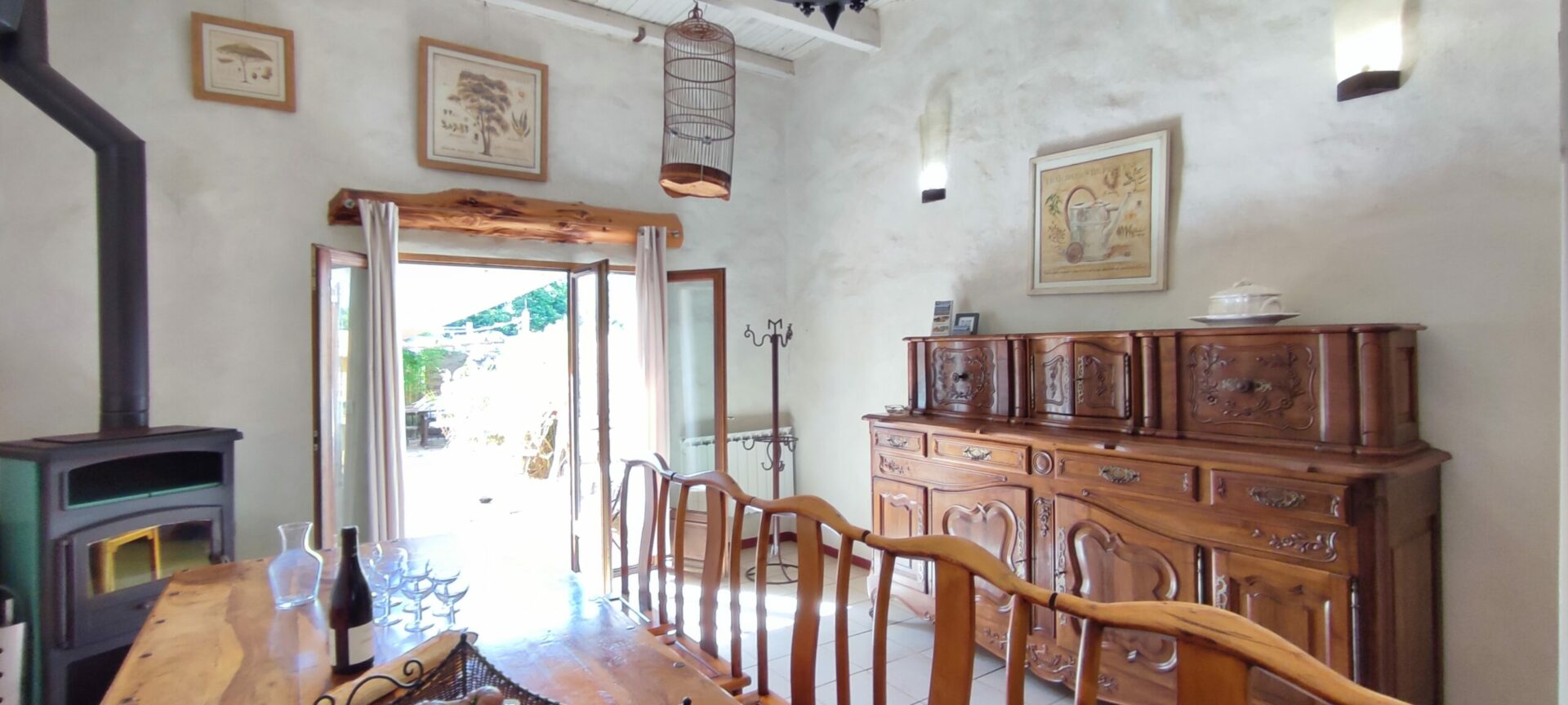 Grande table en bois avec chaises dépareillées dans le séjour du gîte La Fenière, vue sur un ancien bahut, Le Pradet.