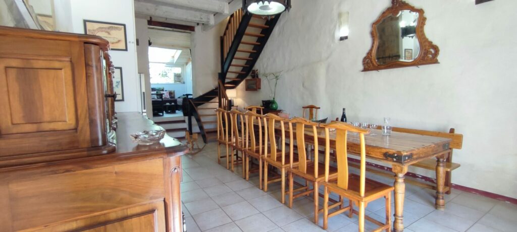 Grande salle à manger ouverte sur le salon du gîte La Fenière, avec table en bois et escalier menant aux chambres, Le Pradet.