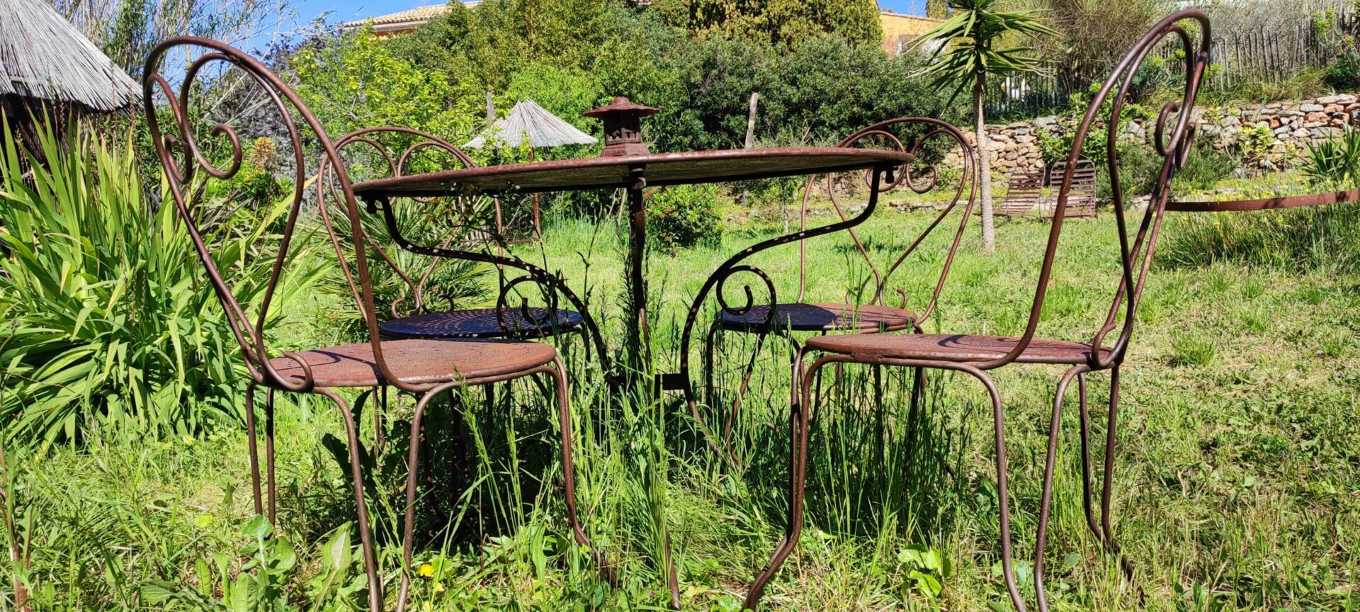 Salon de jardin élégant en fer forgé, comprenant une table et des chaises, installé dans le jardin du Mas de la Gavaresse, illustrant un choix de mobilier durable et sans plastique.