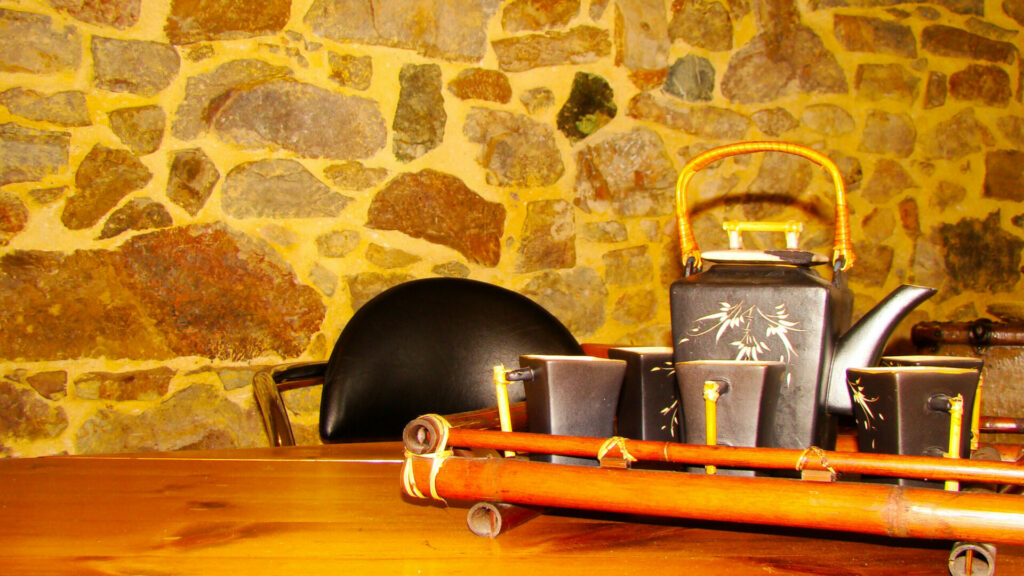 Coin thé cosy avec théière et tasses sur table en bois devant mur de pierres apparentes, représentant l'ambiance du gîte Le Pénéquet.