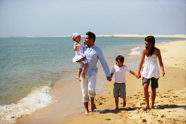 Famille jouant sur une plage de sable fin avec parasol et mer turquoise, vacances en famille, Le Pradet, Var.
