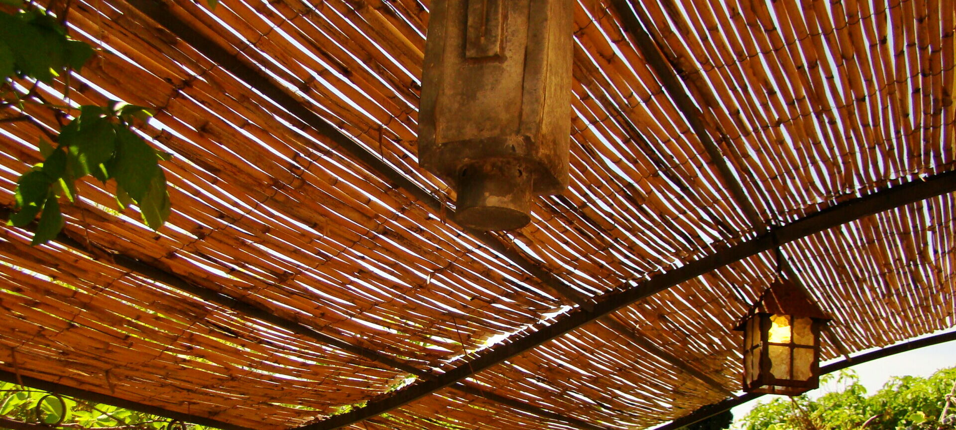 Ancienne lanterne de chemin de fer suspendue sous des canisses en bois sur une terrasse ensoleillée, décoration vintage, charme provençal, Le Pradet.