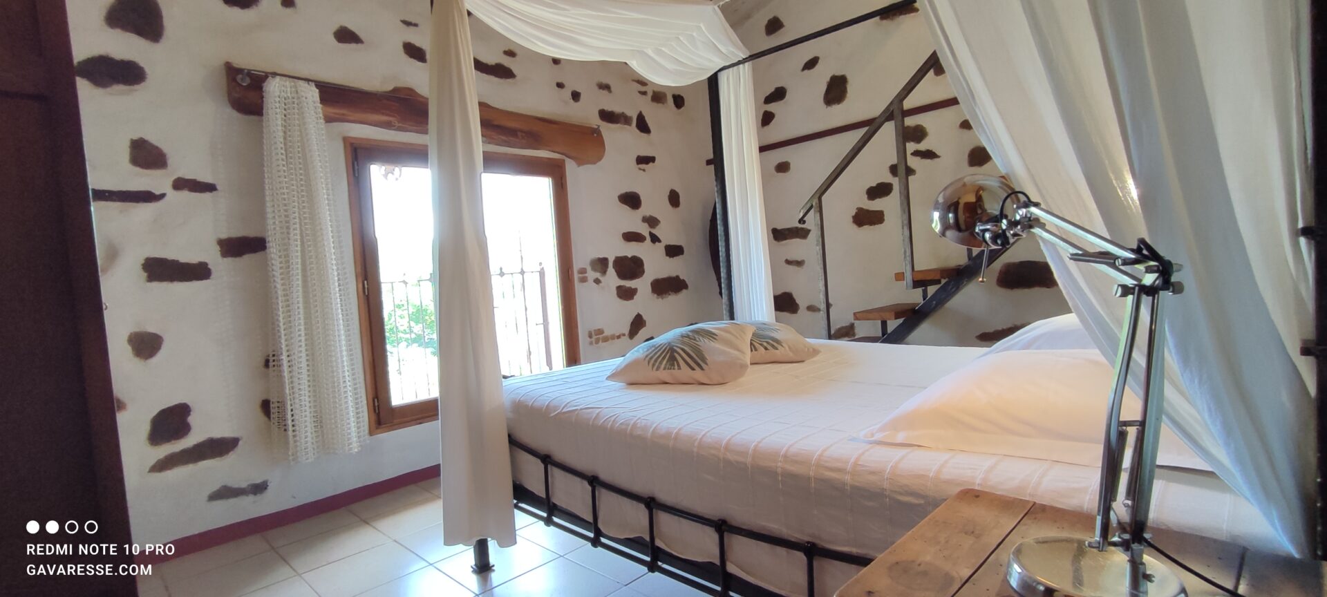 Gros plan sur le baldaquin en bois du lit de la chambre parentale de La Fenière, avec rideaux suspendus, Le Pradet.