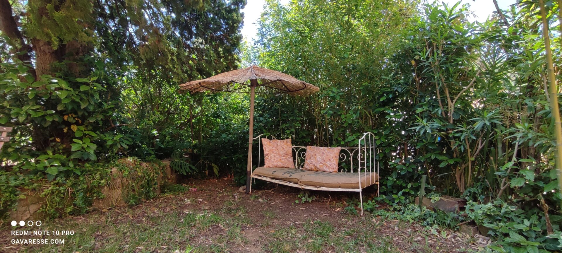 Ancienne banquette en fer forgé avec coussins et parasol en paille dans le jardin du gîte Le Pénéquet, Le Pradet.