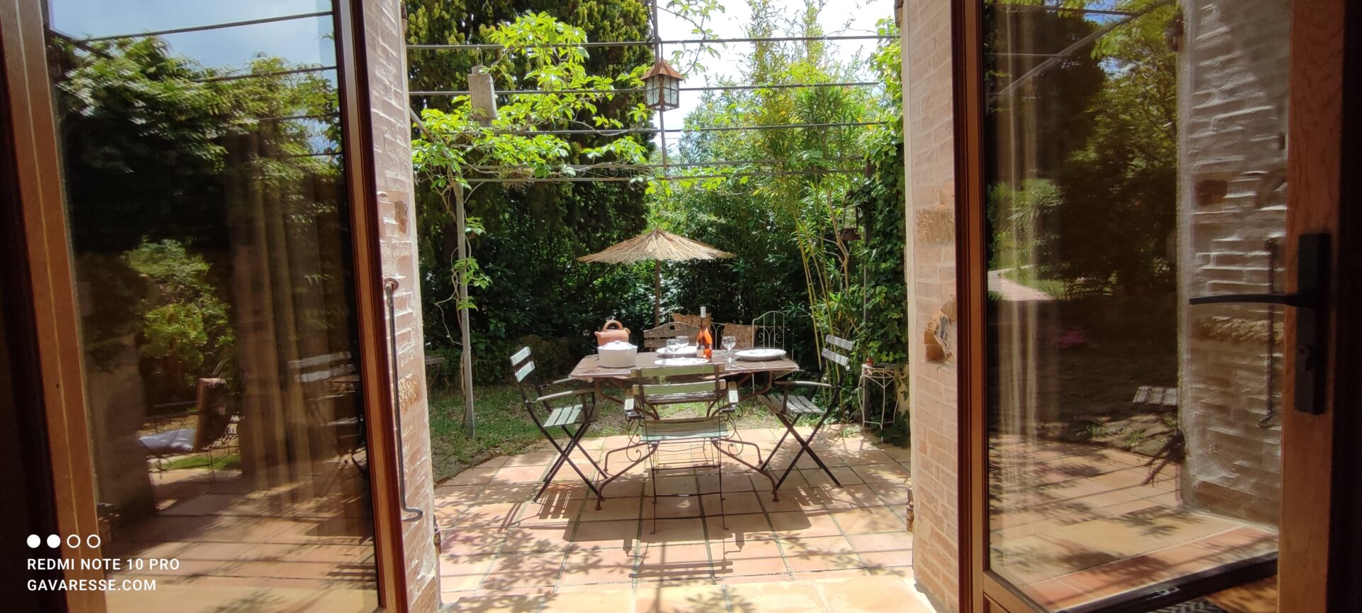 Vue du séjour du gîte Le Pénéquet à travers une grande baie vitrée, donnant sur la terrasse et le jardin, Le Pradet.