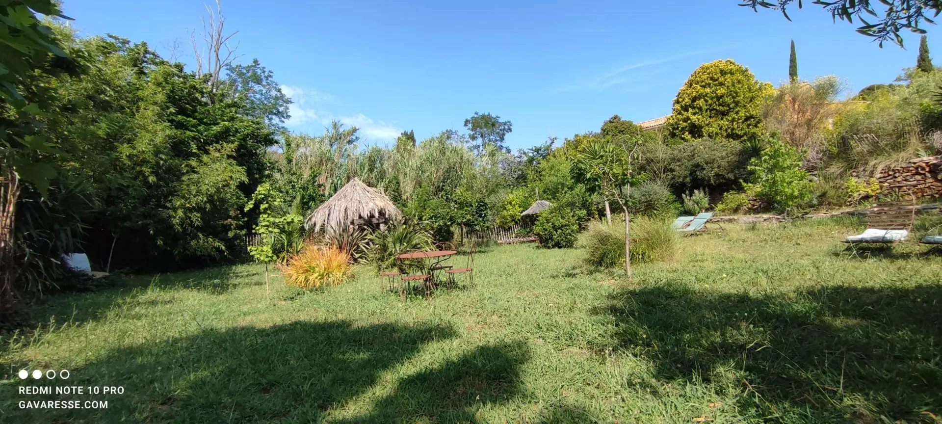 Vue d'ensemble du jardin des locations du Mas de la Gavaresse, avec allées, plantes diverses, ambiance paisible et espaces de détente, reflétant l'éco-responsabilité.